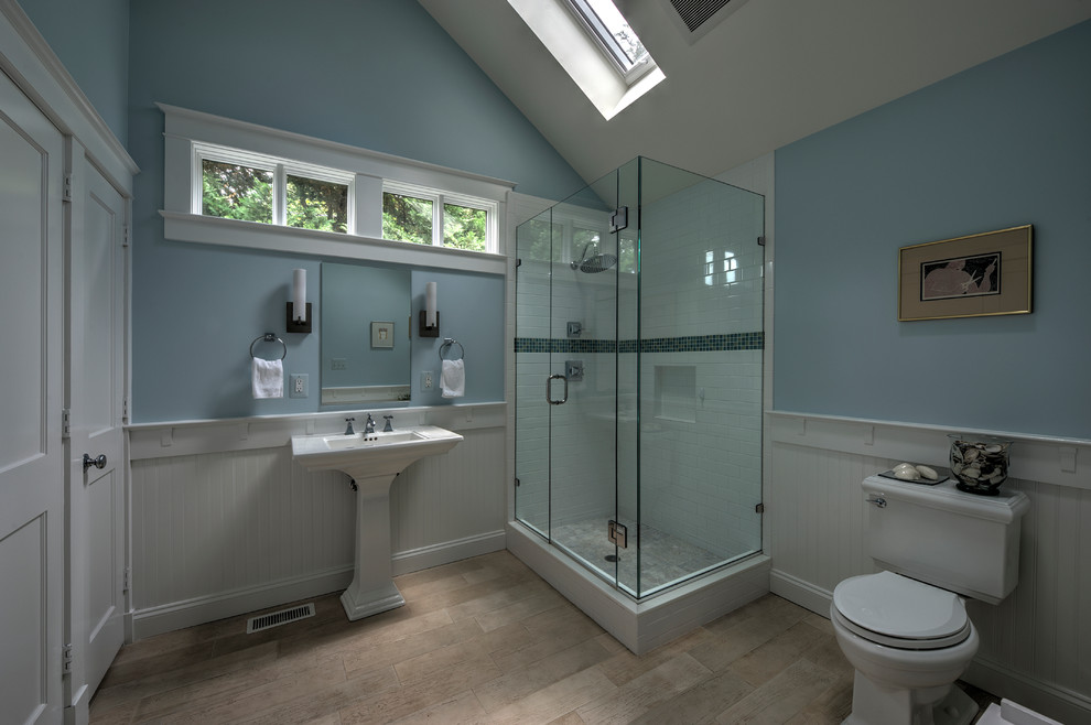 Klassisk inredning av ett mellanstort badrum med dusch, med blå väggar, ljust trägolv, en hörndusch, ett piedestal handfat, en toalettstol med separat cisternkåpa, vit kakel och tunnelbanekakel
