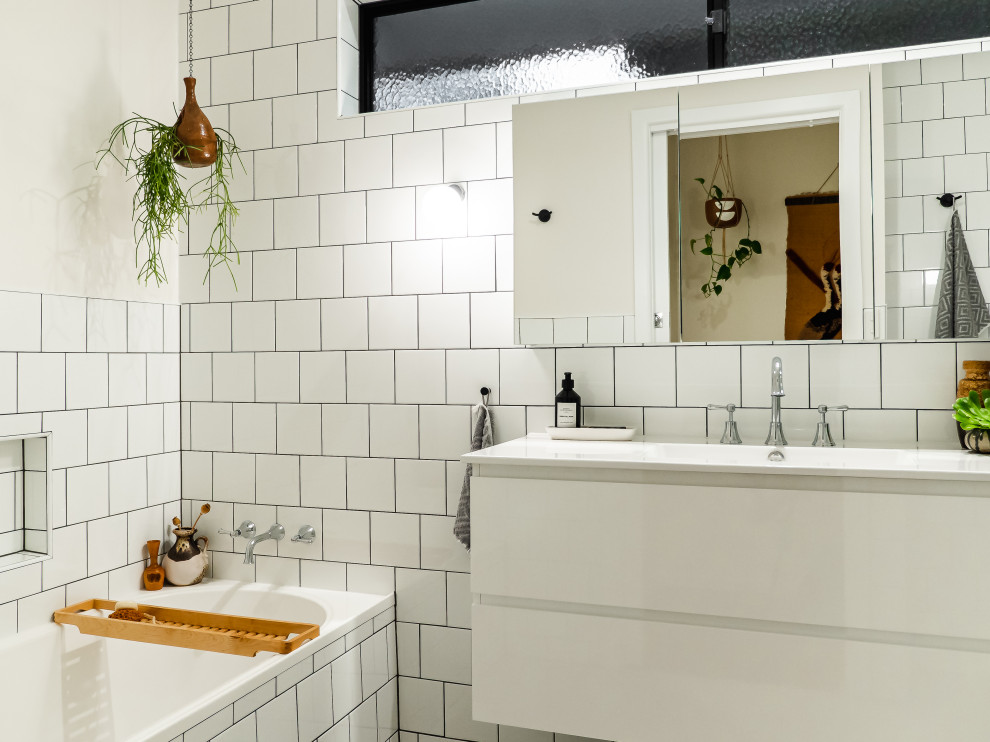 Bild på ett 60 tals vit vitt badrum, med släta luckor, vita skåp, ett badkar i en alkov, vit kakel, tunnelbanekakel, ett integrerad handfat, en öppen dusch, vita väggar, klinkergolv i porslin, bänkskiva i akrylsten och vitt golv