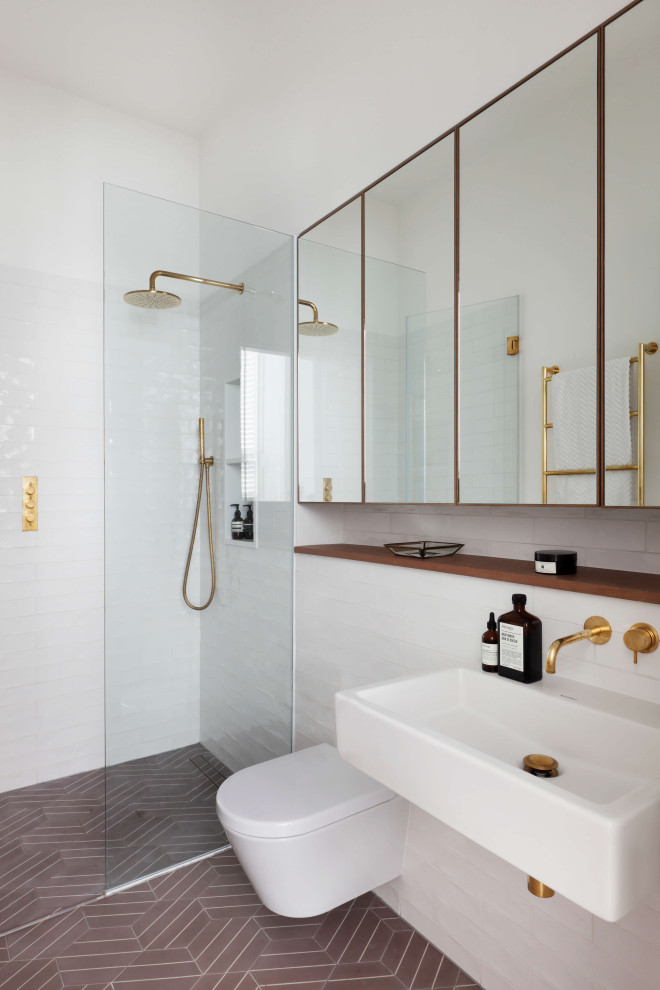 Inredning av ett modernt litet en-suite badrum, med vita skåp, en öppen dusch, en vägghängd toalettstol, grå kakel, keramikplattor, vita väggar, cementgolv, ett väggmonterat handfat, brunt golv och dusch med gångjärnsdörr