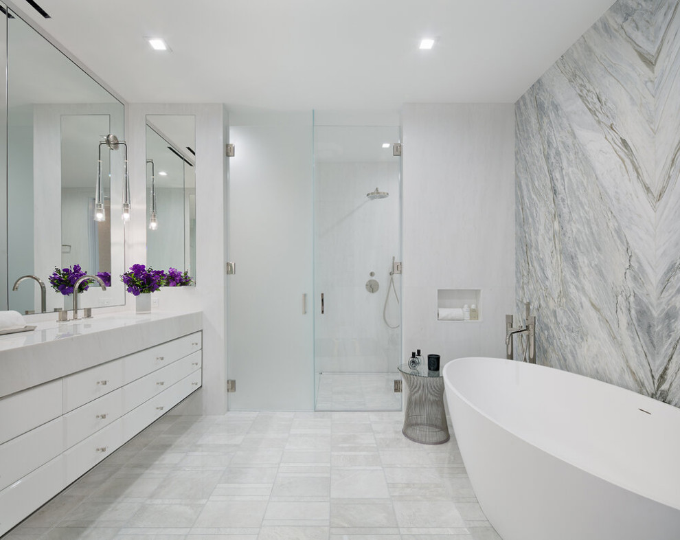 Стильный дизайн: большая главная ванная комната в стиле модернизм с фасадами островного типа, белыми фасадами, отдельно стоящей ванной, душем без бортиков, унитазом-моноблоком, разноцветной плиткой, керамической плиткой, белыми стенами, мраморным полом, монолитной раковиной, мраморной столешницей, белым полом, душем с распашными дверями, белой столешницей, тумбой под две раковины и встроенной тумбой - последний тренд