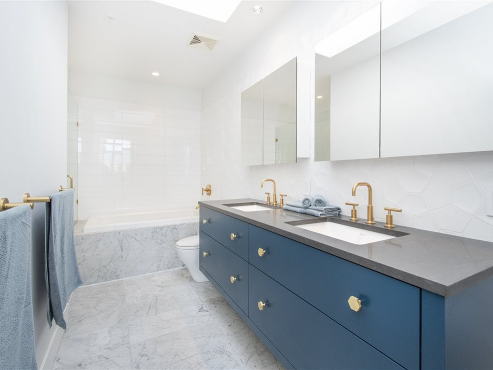 This is an example of a contemporary ensuite bathroom in Vancouver with flat-panel cabinets, blue cabinets, a built-in bath, a one-piece toilet, white tiles, ceramic tiles, white walls, ceramic flooring, a submerged sink, granite worktops, multi-coloured floors, grey worktops, double sinks and a built in vanity unit.
