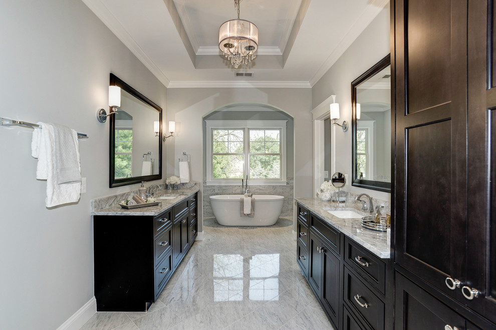 Large traditional ensuite bathroom in DC Metro with a submerged sink, recessed-panel cabinets, dark wood cabinets, marble worktops, a freestanding bath, grey tiles, stone tiles, grey walls and marble flooring.