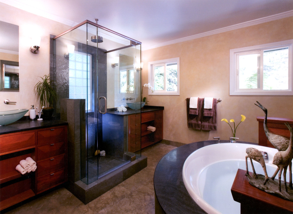 Foto på ett stort funkis en-suite badrum, med ett avlångt handfat, släta luckor, skåp i mörkt trä, granitbänkskiva, en jacuzzi, en öppen dusch, svart kakel, rosa väggar, kalkstensgolv och en toalettstol med hel cisternkåpa