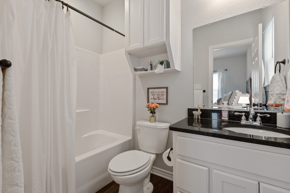 Пример оригинального дизайна: главная ванная комната среднего размера в современном стиле с фасадами в стиле шейкер, белыми фасадами, ванной в нише, душем в нише, унитазом-моноблоком, серыми стенами, темным паркетным полом, врезной раковиной, столешницей из гранита, коричневым полом, шторкой для ванной и черной столешницей