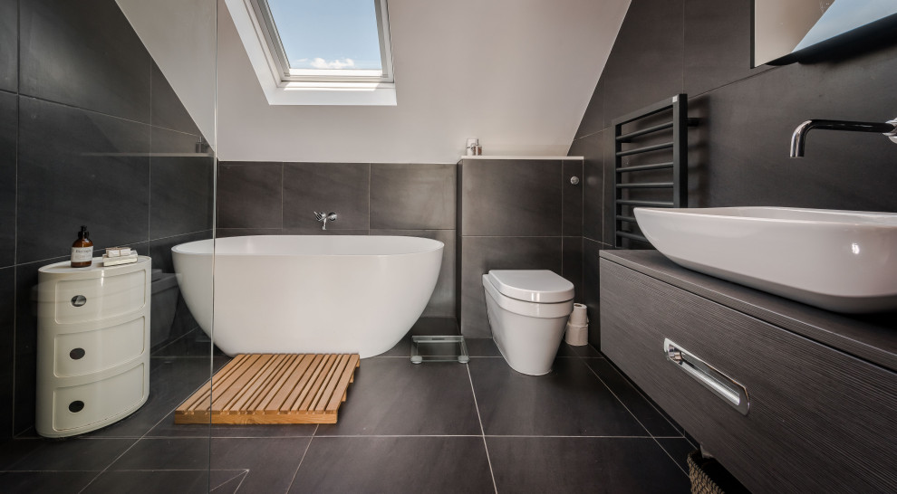 Cette image montre une salle de bain design avec un placard à porte plane, des portes de placard grises, une baignoire indépendante, un carrelage gris, une vasque, un sol gris et un plan de toilette gris.