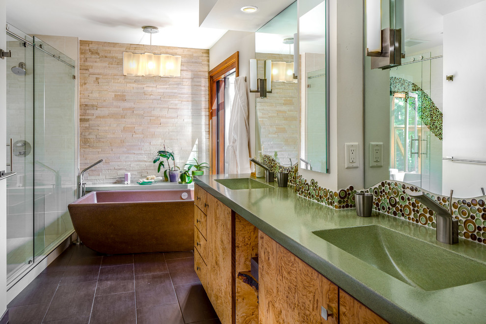 Пример оригинального дизайна: большая главная ванная комната в современном стиле с плоскими фасадами, светлыми деревянными фасадами, отдельно стоящей ванной, душем в нише, унитазом-моноблоком, зеленой плиткой, плиткой из листового стекла, бежевыми стенами, полом из керамогранита, монолитной раковиной и столешницей из бетона