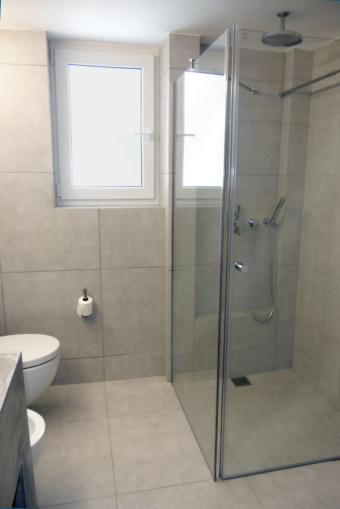 Foto på ett mellanstort funkis badrum med dusch, med ett väggmonterat handfat, släta luckor, skåp i mellenmörkt trä, bänkskiva i betong, en hörndusch, en vägghängd toalettstol, grå kakel, porslinskakel, grå väggar och klinkergolv i porslin