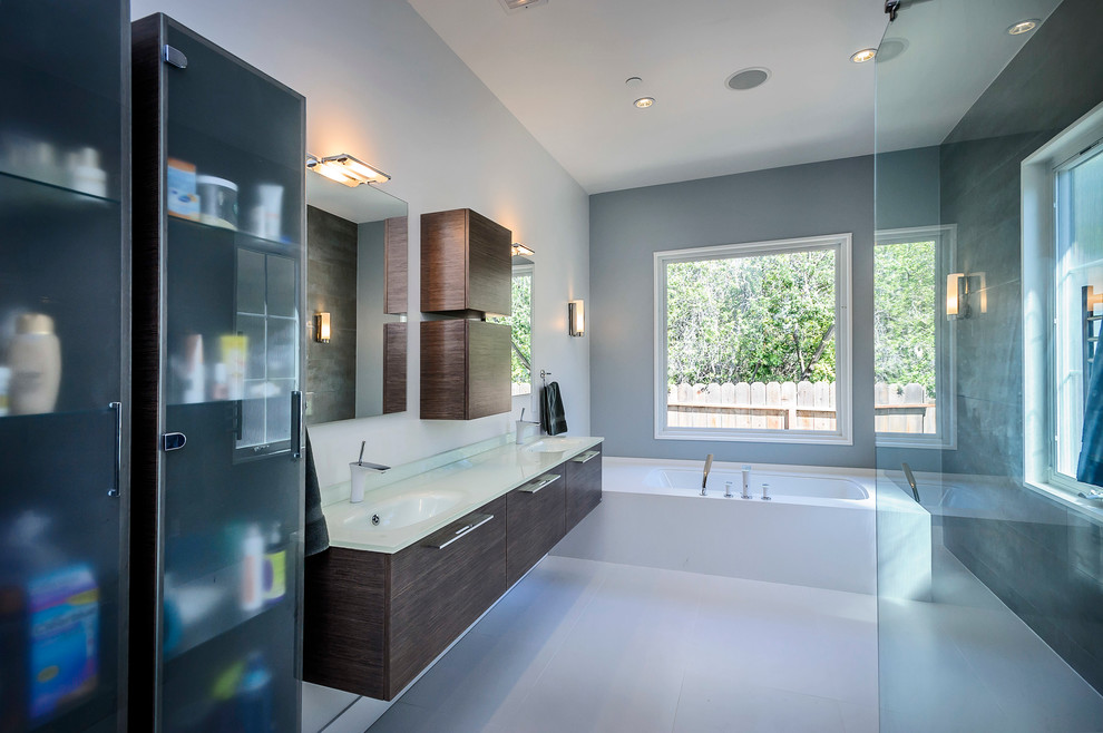 Inredning av ett modernt mellanstort en-suite badrum, med ett integrerad handfat, släta luckor, skåp i mellenmörkt trä, bänkskiva i glas, ett badkar i en alkov, en kantlös dusch och grå väggar