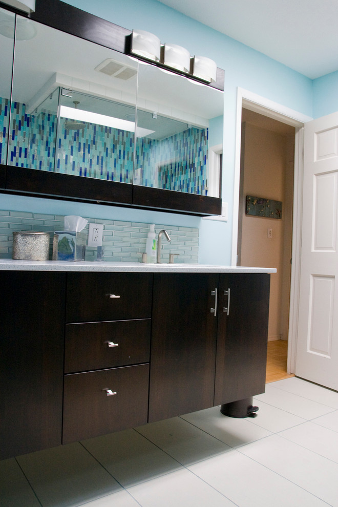 Imagen de cuarto de baño principal minimalista pequeño con armarios con paneles lisos, puertas de armario de madera en tonos medios, encimera de acrílico, bañera exenta, ducha esquinera, sanitario de una pieza, baldosas y/o azulejos azules y paredes azules