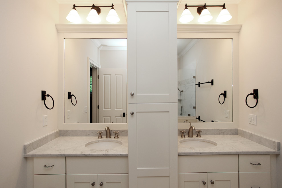 Inredning av ett lantligt badrum, med ett undermonterad handfat, vita skåp, marmorbänkskiva och vita väggar