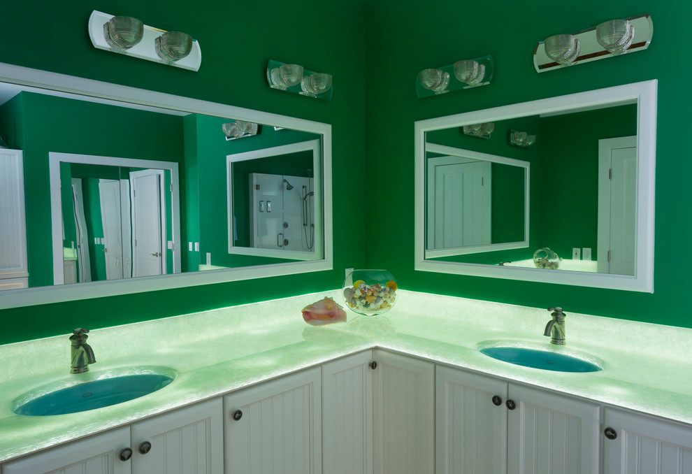 This is an example of a large coastal ensuite bathroom in Charlotte with beaded cabinets, white cabinets, a freestanding bath, a corner shower, stone slabs, green walls, light hardwood flooring, a submerged sink, onyx worktops and green worktops.