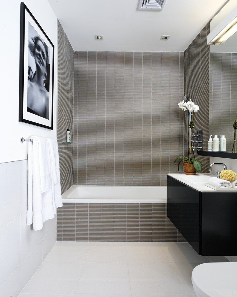 Exemple d'une salle de bain tendance avec un placard à porte plane, des portes de placard noires, une baignoire posée, un combiné douche/baignoire, un carrelage gris, mosaïque et un plan de toilette blanc.