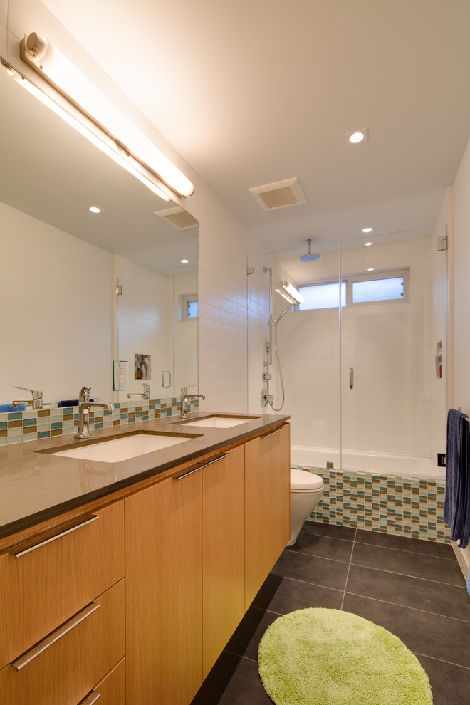 Immagine di una piccola stanza da bagno moderna con lavabo sottopiano, ante lisce, ante in legno chiaro, vasca da incasso, vasca/doccia, WC a due pezzi, piastrelle verdi, pareti bianche e pavimento in gres porcellanato