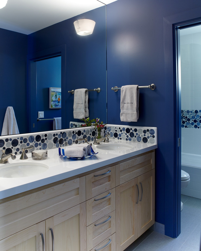 Modelo de cuarto de baño costero pequeño con lavabo bajoencimera, armarios con paneles empotrados, puertas de armario de madera clara, sanitario de dos piezas, baldosas y/o azulejos azules, baldosas y/o azulejos de vidrio, paredes azules y suelo de baldosas de porcelana