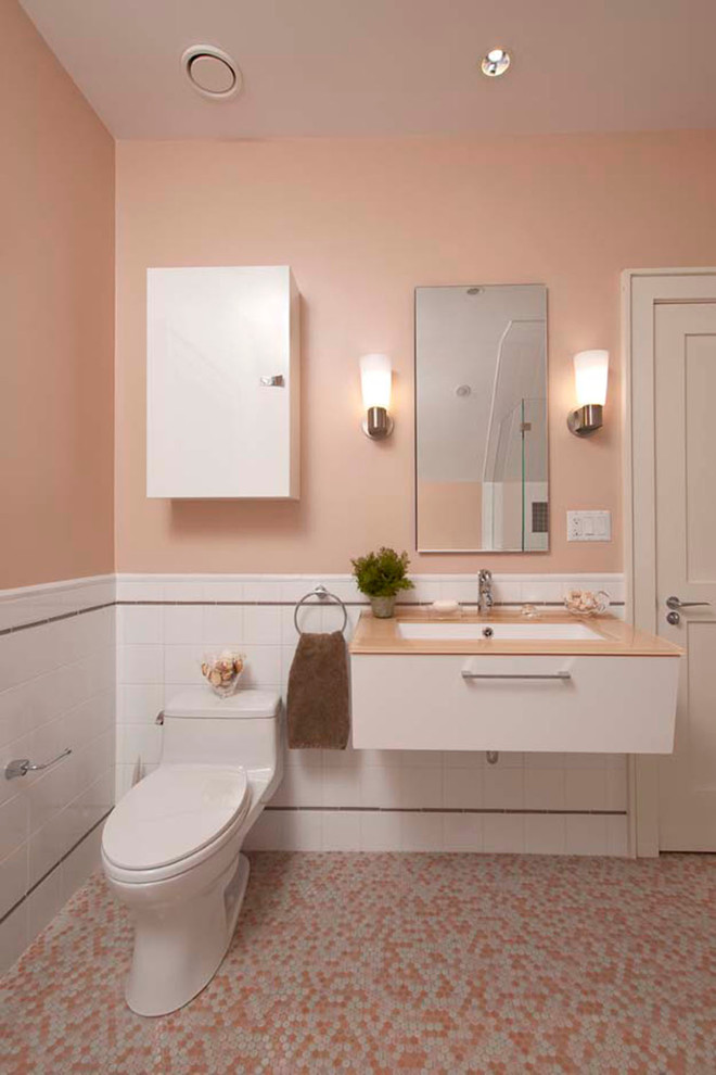 This is an example of a medium sized contemporary bathroom in Providence with flat-panel cabinets, white cabinets, a two-piece toilet, white tiles, ceramic tiles, pink walls, mosaic tile flooring and a submerged sink.