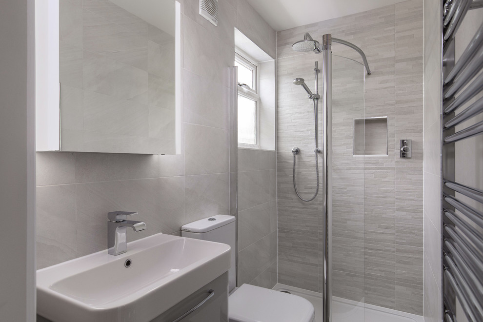 Modernes Duschbad mit flächenbündigen Schrankfronten, grauen Schränken, bodengleicher Dusche, Wandtoilette mit Spülkasten, grauen Fliesen, integriertem Waschbecken, offener Dusche und weißer Waschtischplatte in London