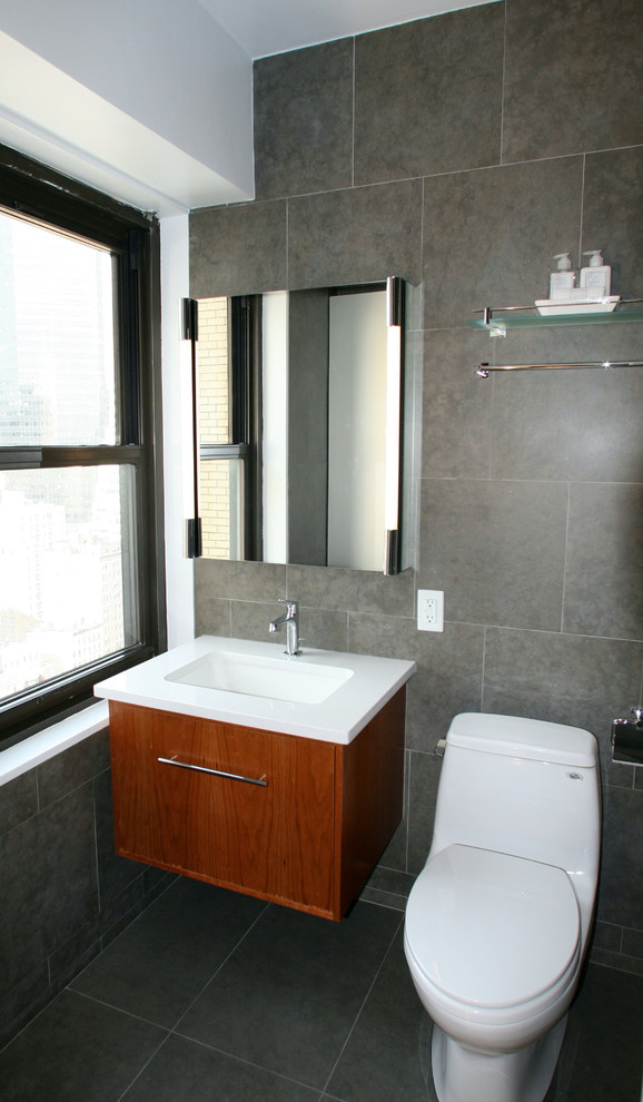 Photo of a medium sized industrial ensuite bathroom in New York with a submerged sink, flat-panel cabinets, medium wood cabinets, engineered stone worktops, a shower/bath combination, a one-piece toilet, grey tiles, porcelain tiles, grey walls, porcelain flooring, grey floors, an open shower, an alcove bath, white worktops, a shower bench, a single sink, a floating vanity unit and a vaulted ceiling.