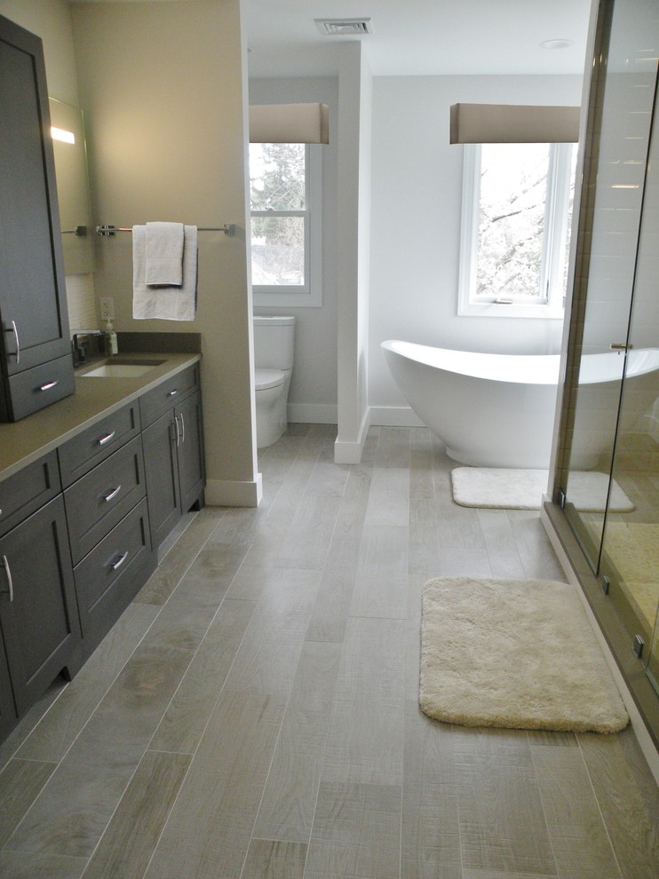 Exemple d'une salle de bain principale moderne en bois foncé avec une baignoire indépendante, une douche double, WC à poser, un mur gris, un sol en carrelage de céramique, un lavabo encastré, un placard à porte shaker, un carrelage gris, des carreaux de céramique et un plan de toilette en quartz.