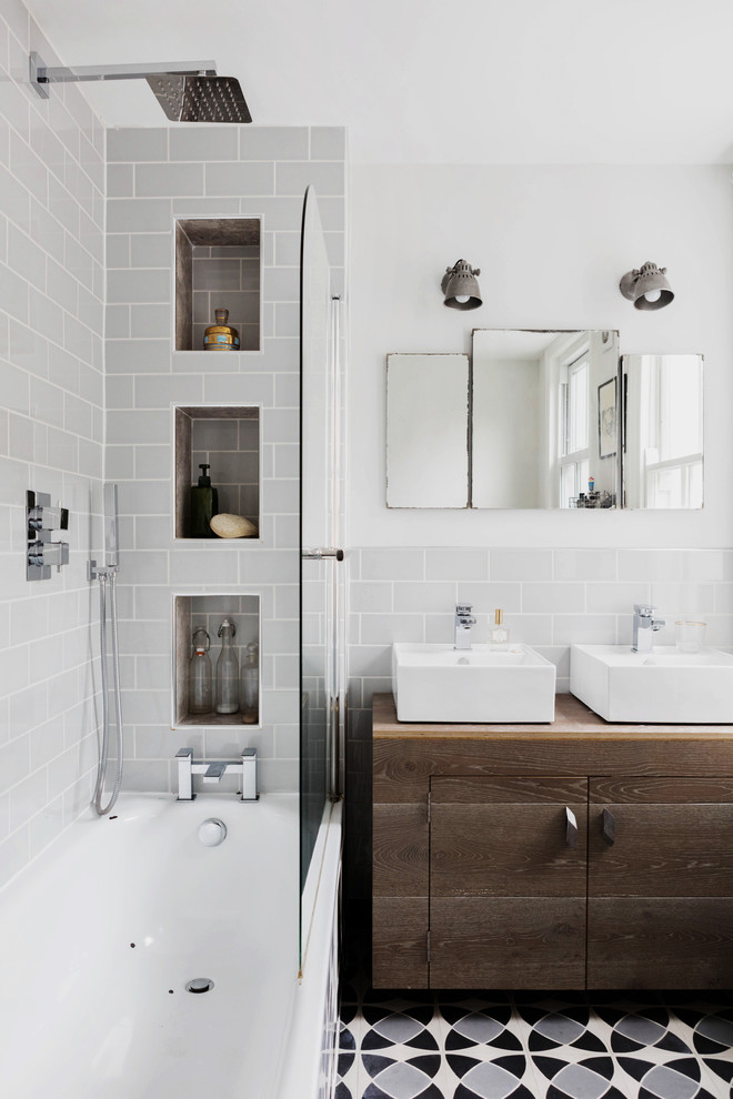 На фото: ванная комната в стиле неоклассика (современная классика) с плоскими фасадами, темными деревянными фасадами, ванной в нише, душем над ванной, серой плиткой, плиткой кабанчик, белыми стенами, настольной раковиной и открытым душем с