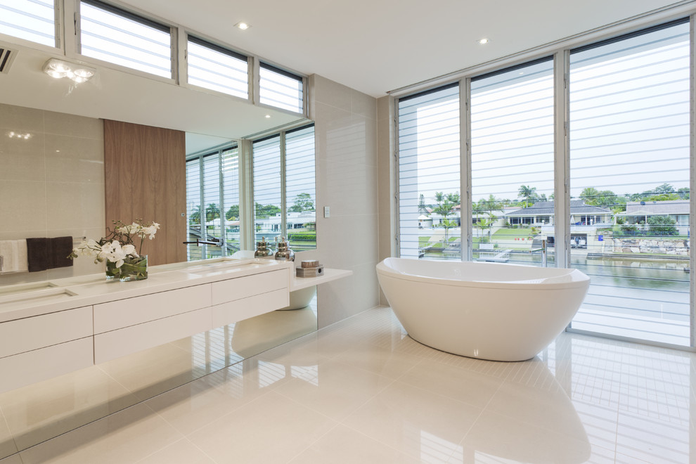 Idée de décoration pour une salle de bain design avec un lavabo encastré, un placard à porte plane, des portes de placard blanches, une baignoire indépendante et un carrelage gris.