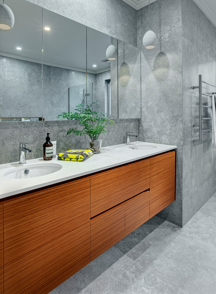 Modelo de cuarto de baño principal contemporáneo de tamaño medio con puertas de armario de madera oscura, bañera exenta, ducha abierta, paredes grises, lavabo bajoencimera y sanitario de una pieza