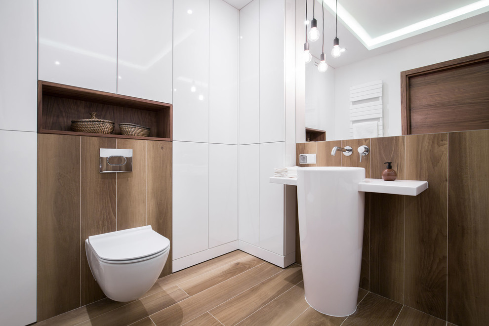 Inspiration för moderna vitt badrum, med släta luckor, vita skåp, en vägghängd toalettstol, brun kakel, vita väggar, ett piedestal handfat och brunt golv