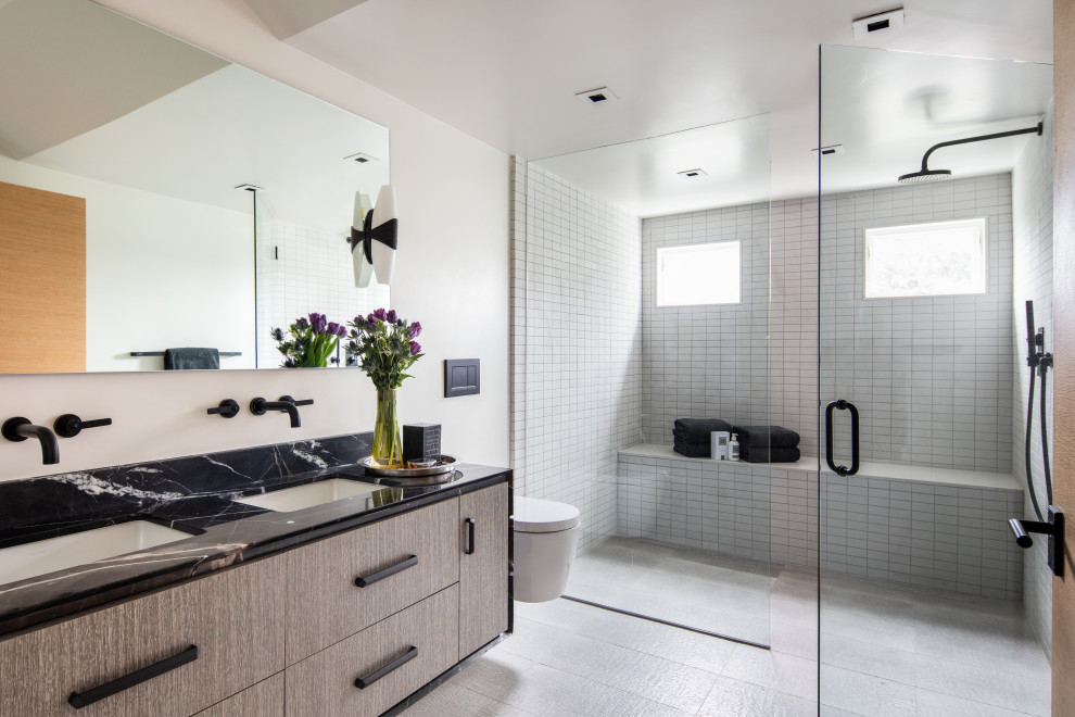 Example of a large trendy white tile double-sink and gray floor bathroom design in San Francisco with flat-panel cabinets, marble countertops, black countertops, a floating vanity, gray cabinets, white walls, an undermount sink and a hinged shower door