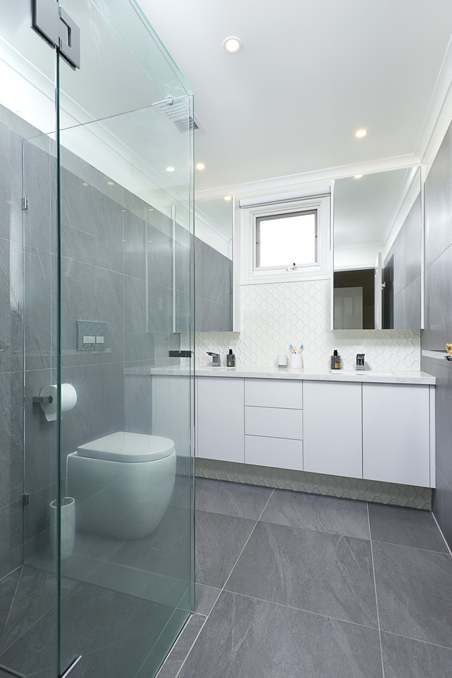 Modern inredning av ett mellanstort vit vitt badrum, med vita skåp, en hörndusch, en vägghängd toalettstol, grå kakel, porslinskakel, grå väggar, klinkergolv i porslin, ett undermonterad handfat, bänkskiva i akrylsten, grått golv och dusch med gångjärnsdörr