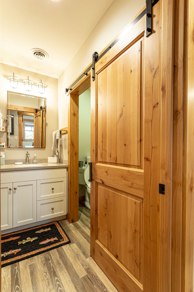 Design ideas for a rustic bathroom in Other with shaker cabinets, white cabinets, a one-piece toilet, white walls, laminate floors, solid surface worktops, brown floors, grey worktops, an enclosed toilet, a single sink and a built in vanity unit.
