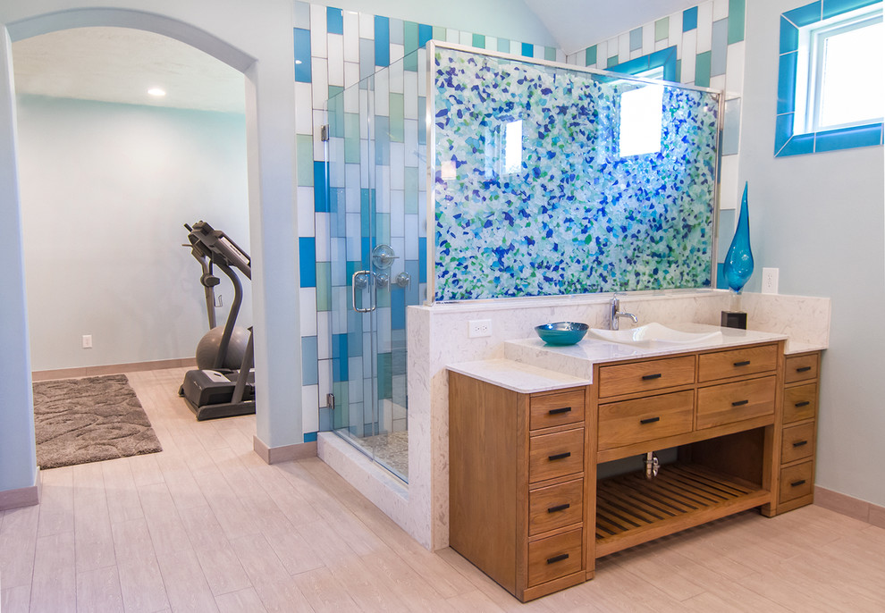 Photo of a large beach style ensuite bathroom in Houston with a vessel sink, flat-panel cabinets, light wood cabinets, limestone worktops, a corner shower, a two-piece toilet, beige tiles, glass tiles, green walls and light hardwood flooring.