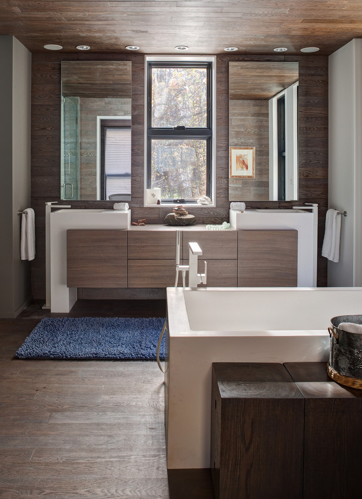 Foto de cuarto de baño principal actual con armarios con paneles lisos, puertas de armario de madera en tonos medios, bañera exenta, suelo de madera oscura y lavabo integrado