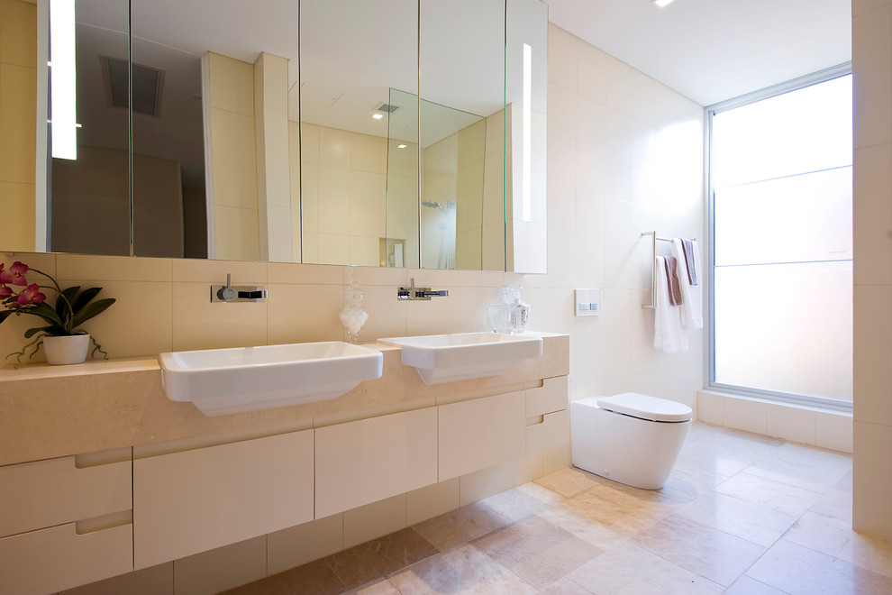 Idee per una stanza da bagno minimal con top in pietra calcarea, pavimento in pietra calcarea, lavabo da incasso, ante di vetro, ante beige, piastrelle beige e piastrelle in pietra