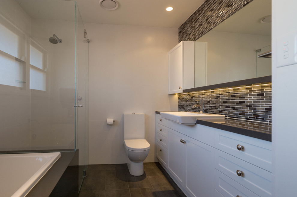 Transitional master multicolored tile brown floor and single-sink drop-in bathtub photo in Other with white cabinets, a hinged shower door, black countertops and a freestanding vanity