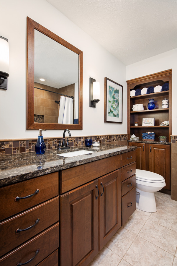 Idée de décoration pour une salle de bain tradition en bois brun de taille moyenne avec un carrelage marron, un lavabo encastré, un placard avec porte à panneau surélevé et un plan de toilette en quartz modifié.