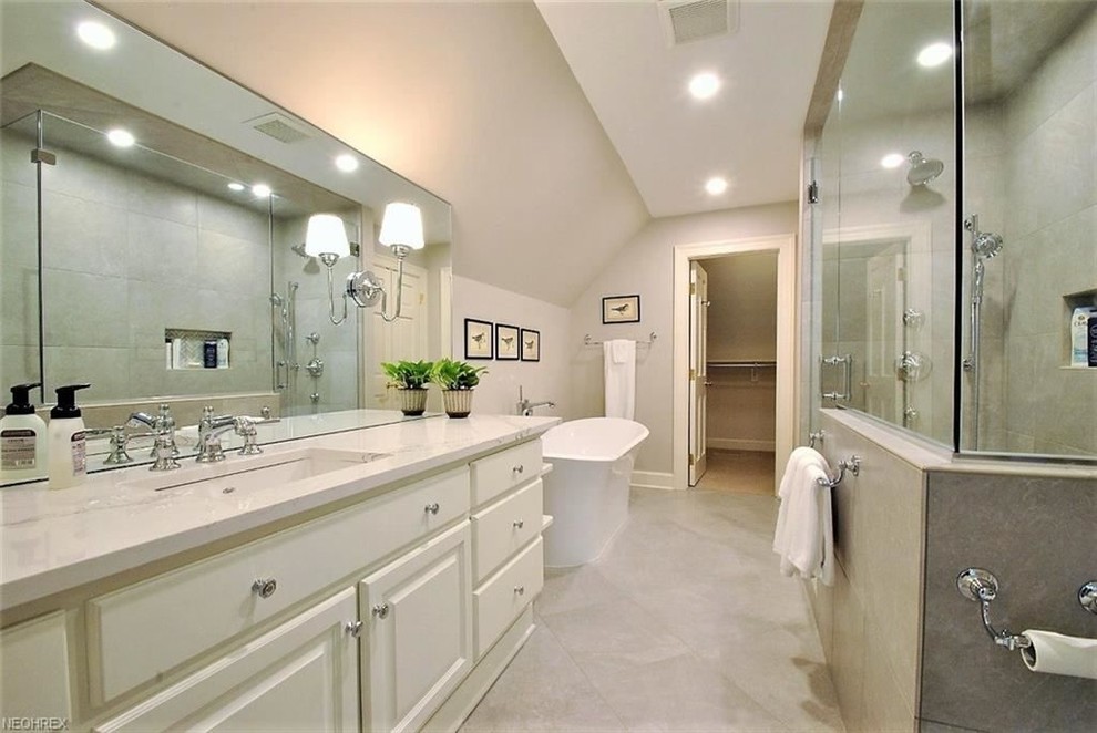 Inredning av ett klassiskt mellanstort grå grått badrum, med luckor med upphöjd panel, vita skåp, ett fristående badkar, en toalettstol med separat cisternkåpa, grå kakel, grå väggar, klinkergolv i porslin, ett undermonterad handfat, bänkskiva i kvarts, grått golv och dusch med gångjärnsdörr