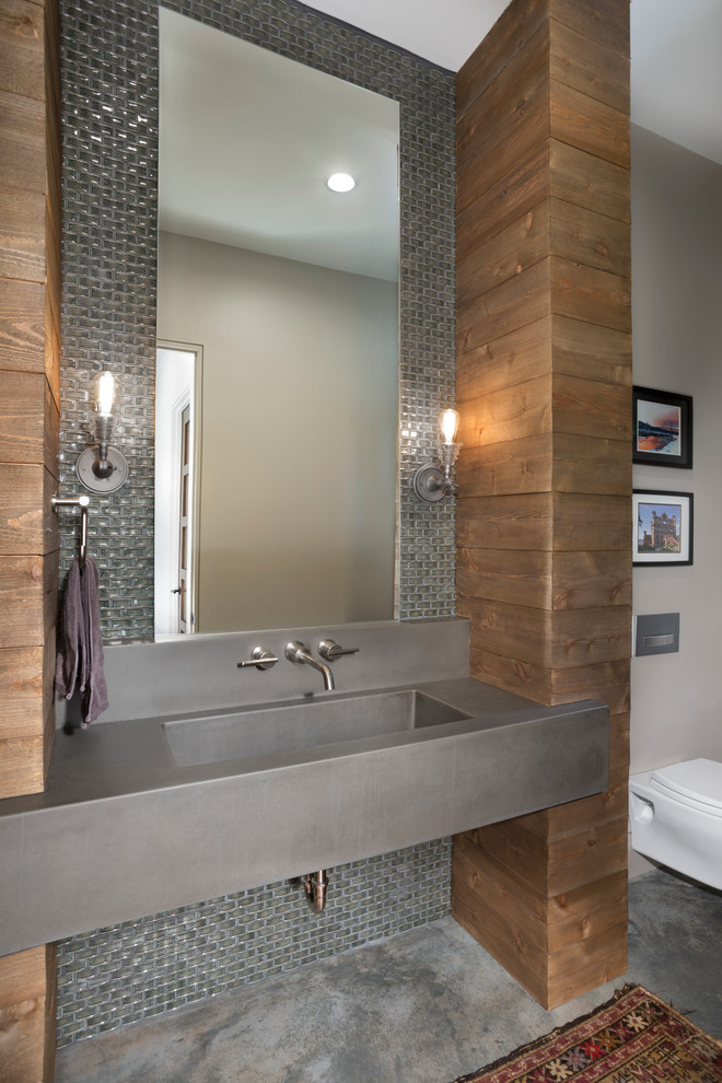 Foto di una stanza da bagno contemporanea con WC sospeso, piastrelle grigie, piastrelle di vetro, pareti grigie, pavimento in cemento, lavabo integrato e top in cemento