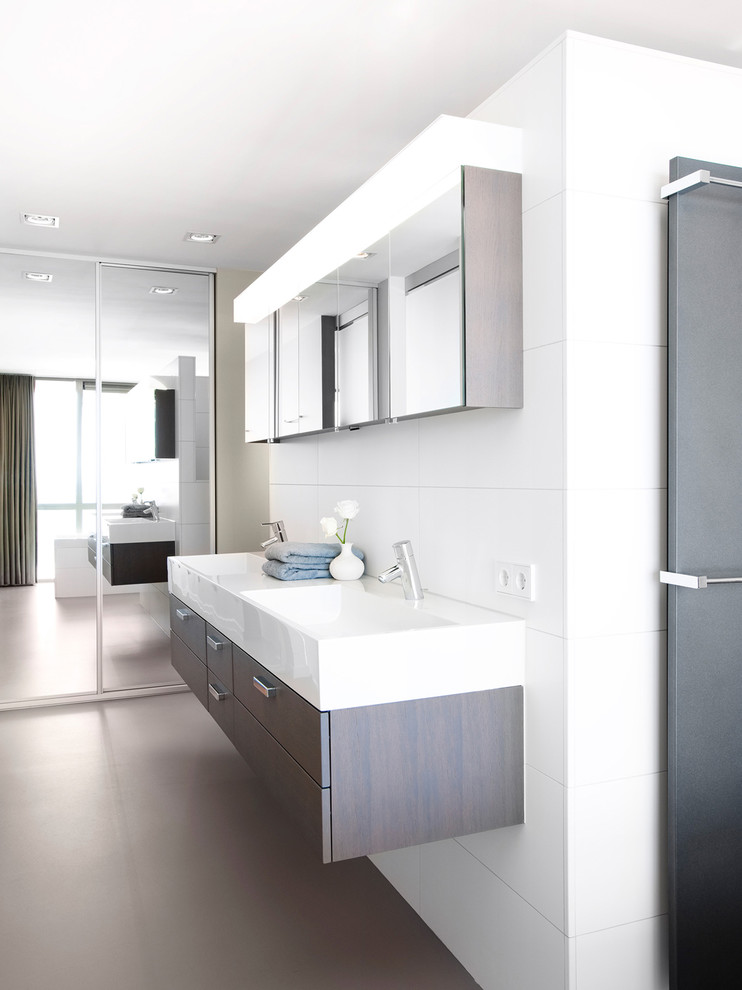 Réalisation d'une salle de bain minimaliste en bois foncé avec un lavabo suspendu, un placard à porte plane et un carrelage blanc.