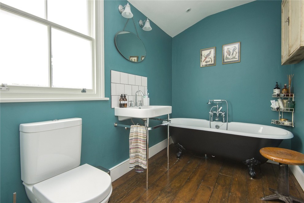 Foto de cuarto de baño clásico de tamaño medio con bañera con patas, sanitario de dos piezas, baldosas y/o azulejos de cemento, paredes azules, suelo de madera oscura, lavabo tipo consola y suelo marrón