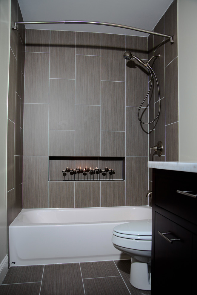 Modern inredning av ett litet en-suite badrum, med släta luckor, skåp i mörkt trä, marmorbänkskiva, en dusch/badkar-kombination, en toalettstol med separat cisternkåpa, grå kakel, porslinskakel, vita väggar och klinkergolv i porslin