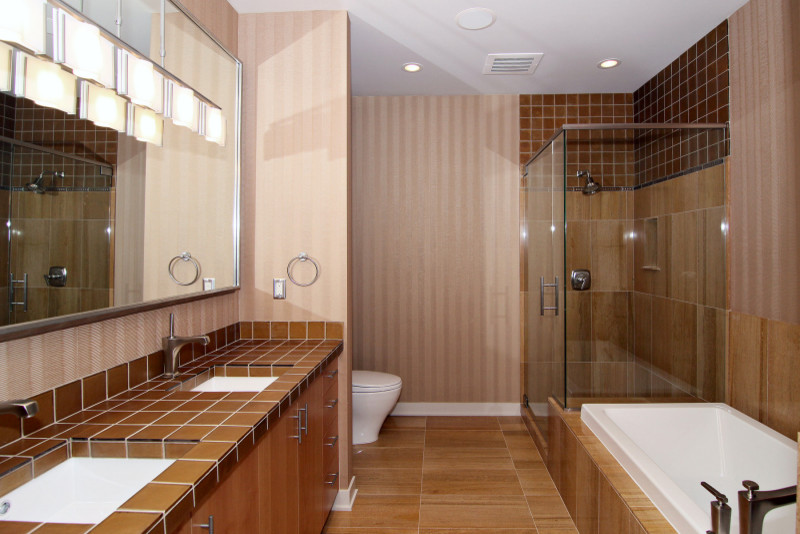 Photo of a large modern ensuite bathroom in Minneapolis with flat-panel cabinets, medium wood cabinets, a built-in bath, a submerged sink and glass worktops.
