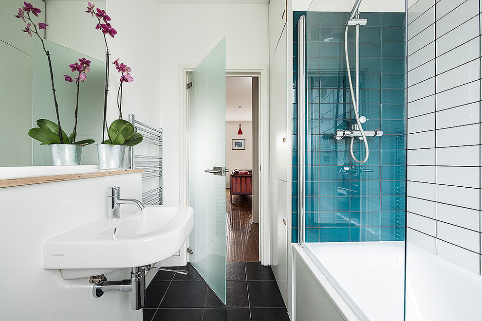 This is an example of a small contemporary bathroom in London with a wall-mounted sink, flat-panel cabinets, white cabinets, wooden worktops, a built-in bath, a shower/bath combination, a wall mounted toilet, blue tiles, ceramic tiles, white walls and ceramic flooring.