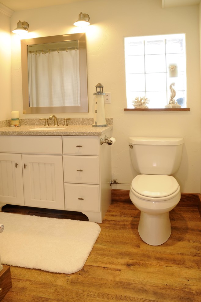 Cette image montre une salle d'eau marine avec un lavabo encastré, des portes de placard blanches, WC séparés, un mur blanc et un sol en bois brun.