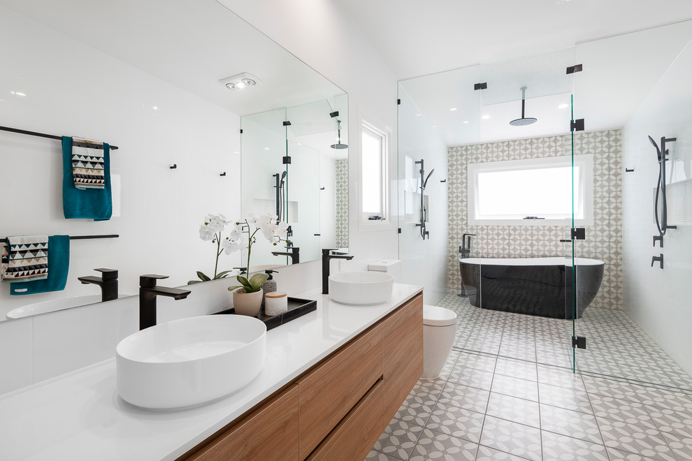 Идея дизайна: огромная детская ванная комната в современном стиле с светлыми деревянными фасадами, отдельно стоящей ванной, душевой комнатой, унитазом-моноблоком, серой плиткой, керамогранитной плиткой, серыми стенами, полом из керамогранита, настольной раковиной, столешницей из искусственного кварца, серым полом, душем с распашными дверями и белой столешницей