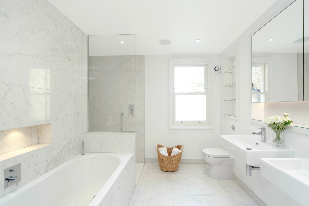 Modern inredning av ett mellanstort badrum, med ett platsbyggt badkar, en öppen dusch, vit kakel, ett väggmonterat handfat, släta luckor, en toalettstol med hel cisternkåpa, vita väggar, marmorgolv och med dusch som är öppen