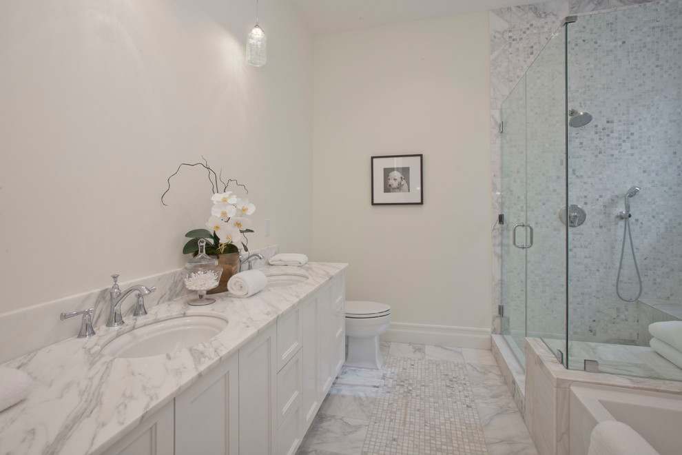 Inspiration for a mid-sized transitional master white tile and marble tile marble floor and white floor bathroom remodel in Los Angeles with recessed-panel cabinets, white cabinets, a one-piece toilet, white walls, an undermount sink, marble countertops, a hinged shower door and white countertops