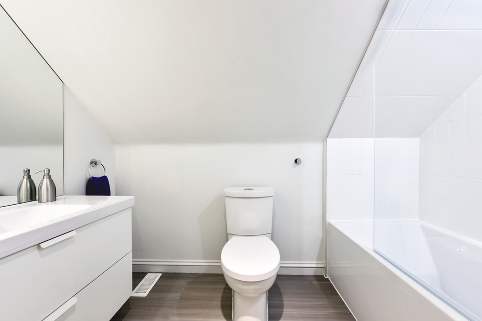 Inspiration for a small contemporary shower room bathroom in Ottawa with flat-panel cabinets, white cabinets, a corner bath, a shower/bath combination, a one-piece toilet, white tiles, ceramic tiles, white walls, medium hardwood flooring, an integrated sink and solid surface worktops.