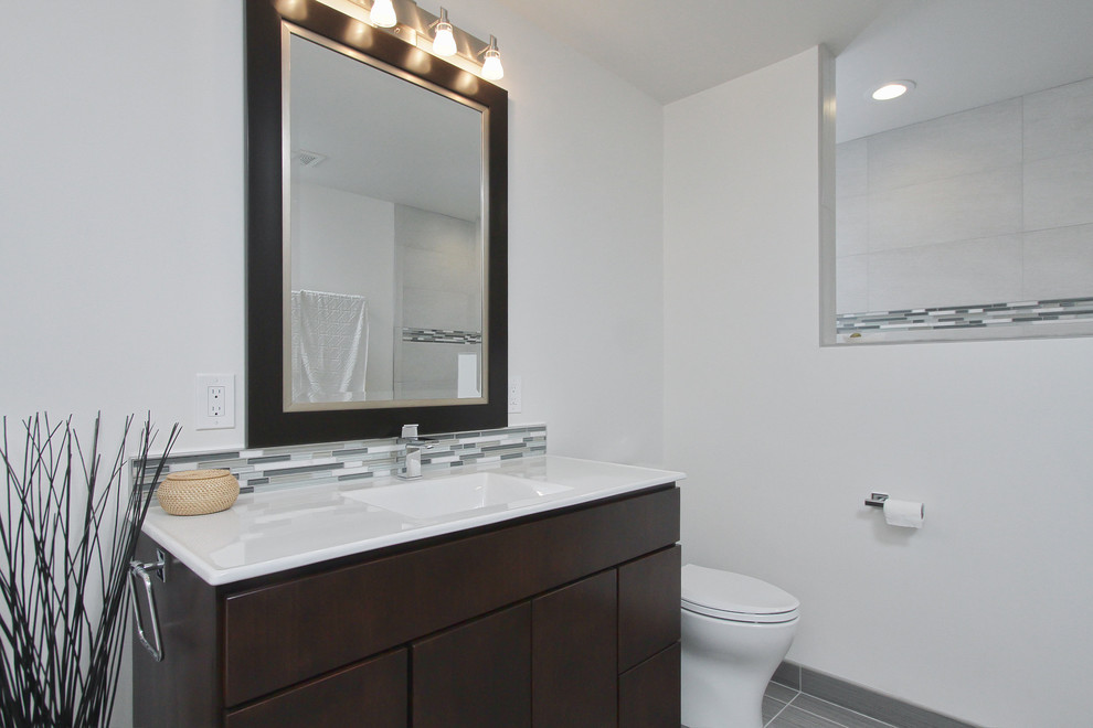 This is an example of a medium sized ensuite bathroom in Philadelphia with flat-panel cabinets, dark wood cabinets, a freestanding bath, an alcove shower, a two-piece toilet, black and white tiles, grey tiles, multi-coloured tiles, pebble tiles, white walls, ceramic flooring, an integrated sink and solid surface worktops.