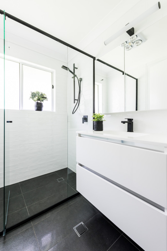 Idéer för ett mellanstort modernt vit badrum med dusch, med släta luckor, vita skåp, en dusch i en alkov, vit kakel, vita väggar, ett integrerad handfat, svart golv och dusch med gångjärnsdörr