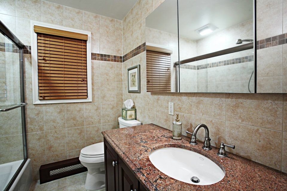 Пример оригинального дизайна: ванная комната в классическом стиле с врезной раковиной, фасадами с выступающей филенкой, темными деревянными фасадами, столешницей из гранита, ванной в нише, душем над ванной, унитазом-моноблоком, бежевой плиткой и каменной плиткой