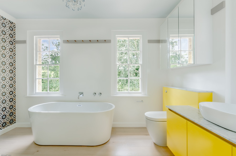 Идея дизайна: детская ванная комната среднего размера в стиле фьюжн с плоскими фасадами, желтыми фасадами, отдельно стоящей ванной, угловым душем, унитазом-моноблоком, разноцветной плиткой, керамогранитной плиткой, белыми стенами, светлым паркетным полом, настольной раковиной, мраморной столешницей и душем с распашными дверями
